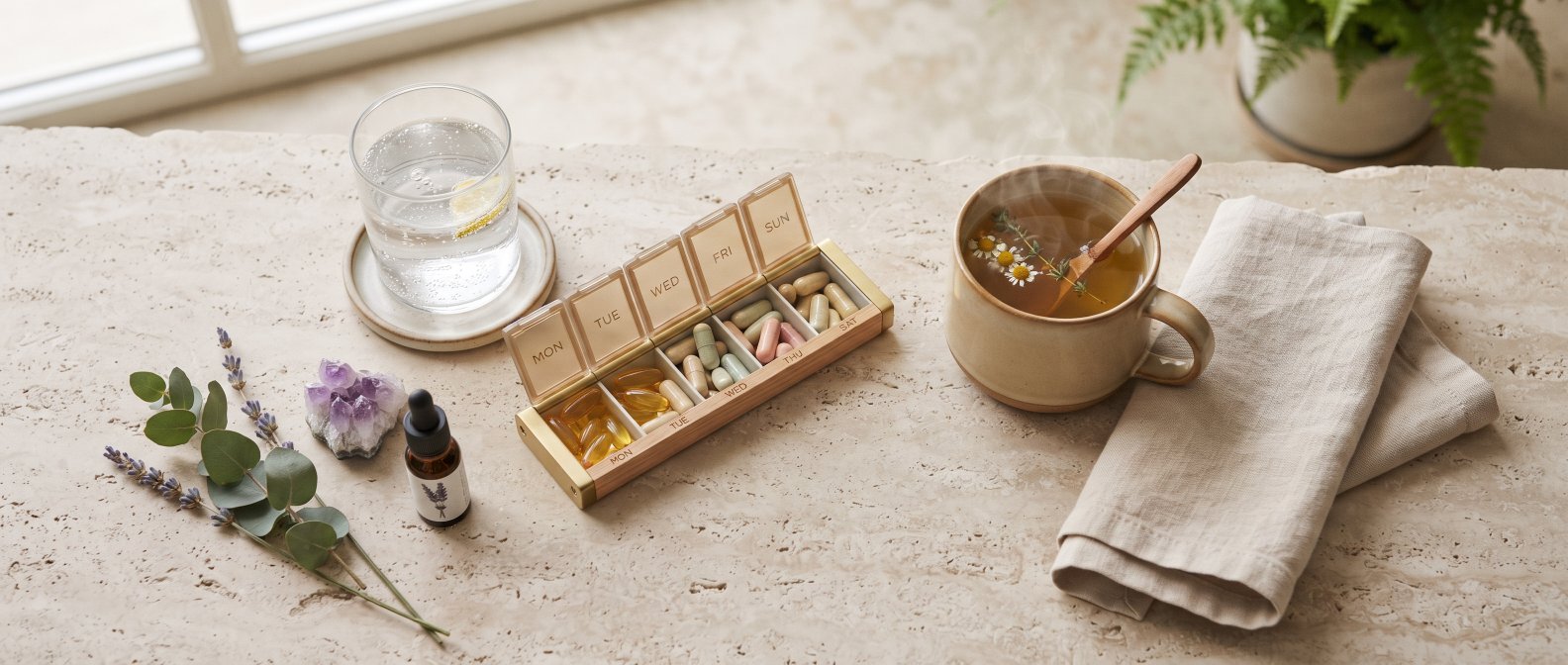 Routine bien-etre, verre d eau, pilulier avec gelules, tasse de tisane et linge sur une surface claire, lumiere douce du matin